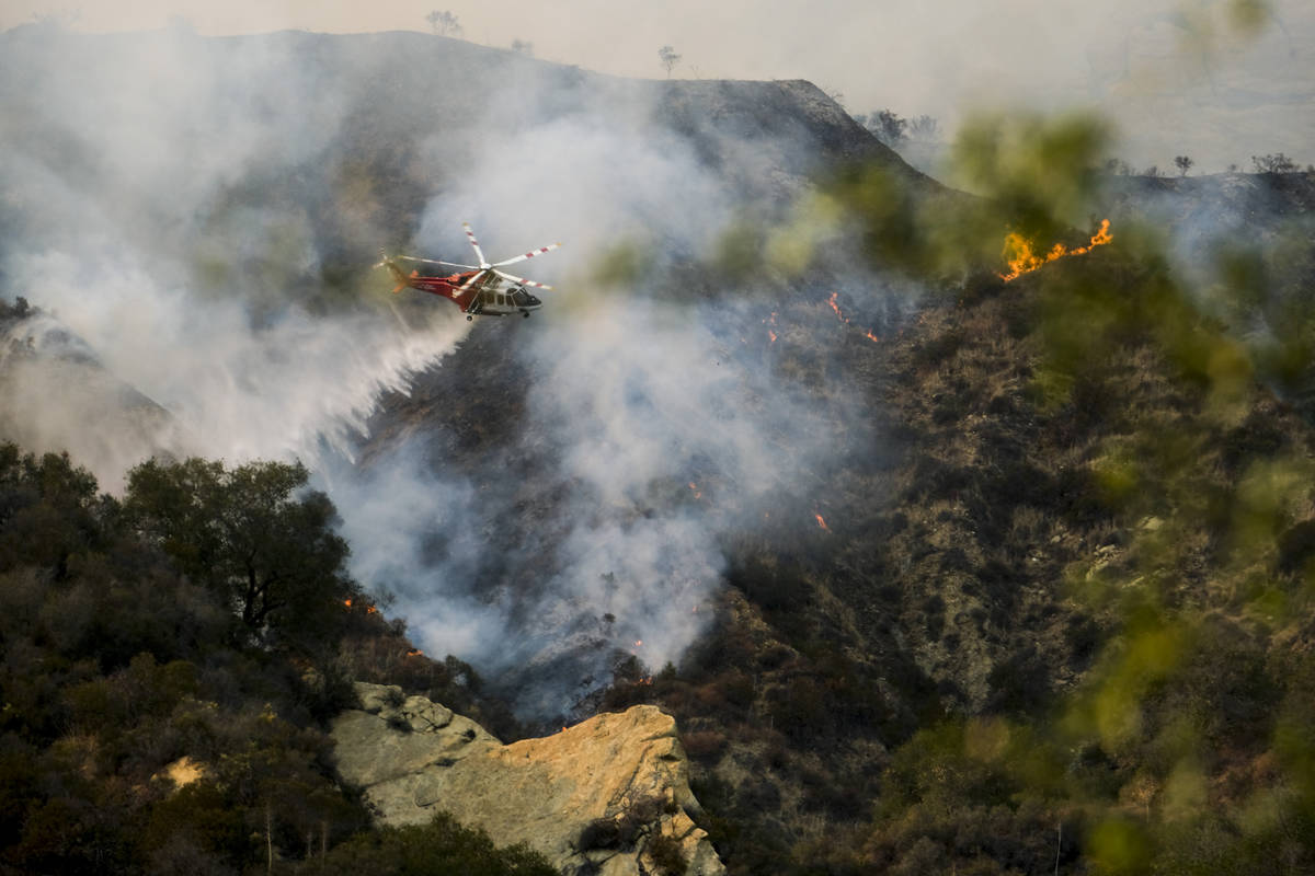 A firefighting helicopter drops water on a brush fire scorching at least 100 acres in the Pacif ...