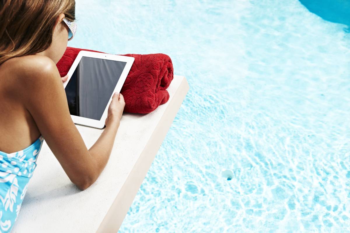 A guest holding an iPad while lounging at a pool. (Courtesy, MGM Resorts International)