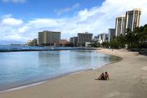 A couple rests on an empty section of Waikiki Beach in Honolulu in March 2020. (AP Photo/Caleb ...