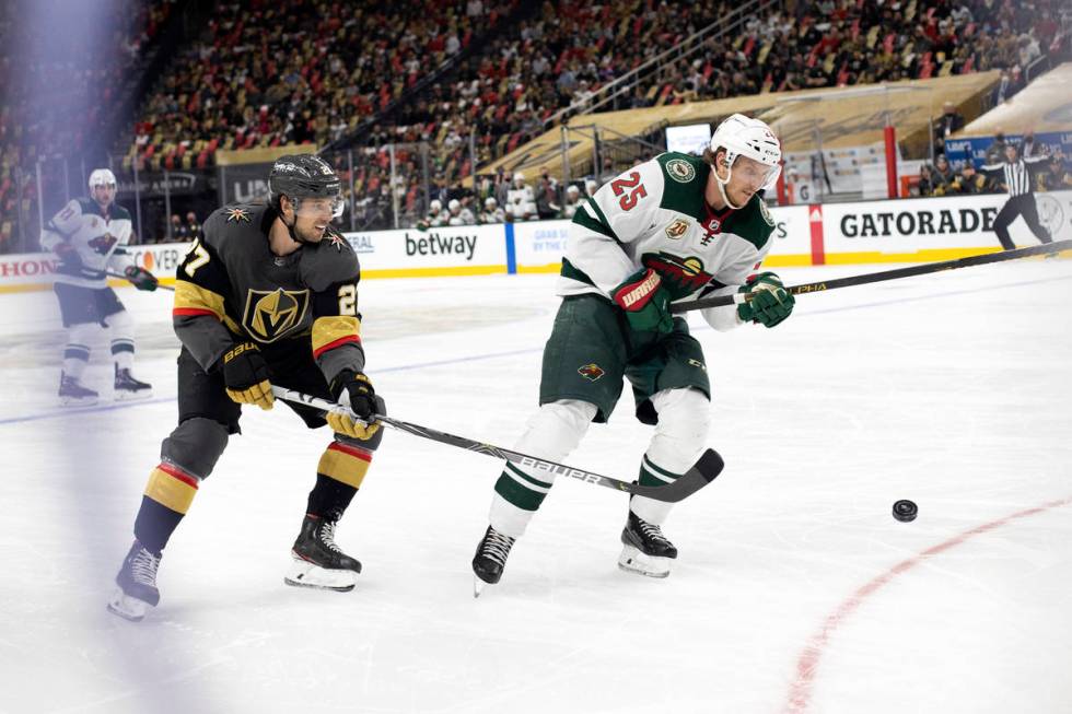 Golden Knights defenseman Shea Theodore (27) and Wild defenseman Jonas Brodin (25) compete for ...