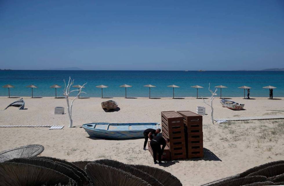 Workers arrange sunbeds as others install umbrellas at Plaka beach on the Aegean island of Naxo ...