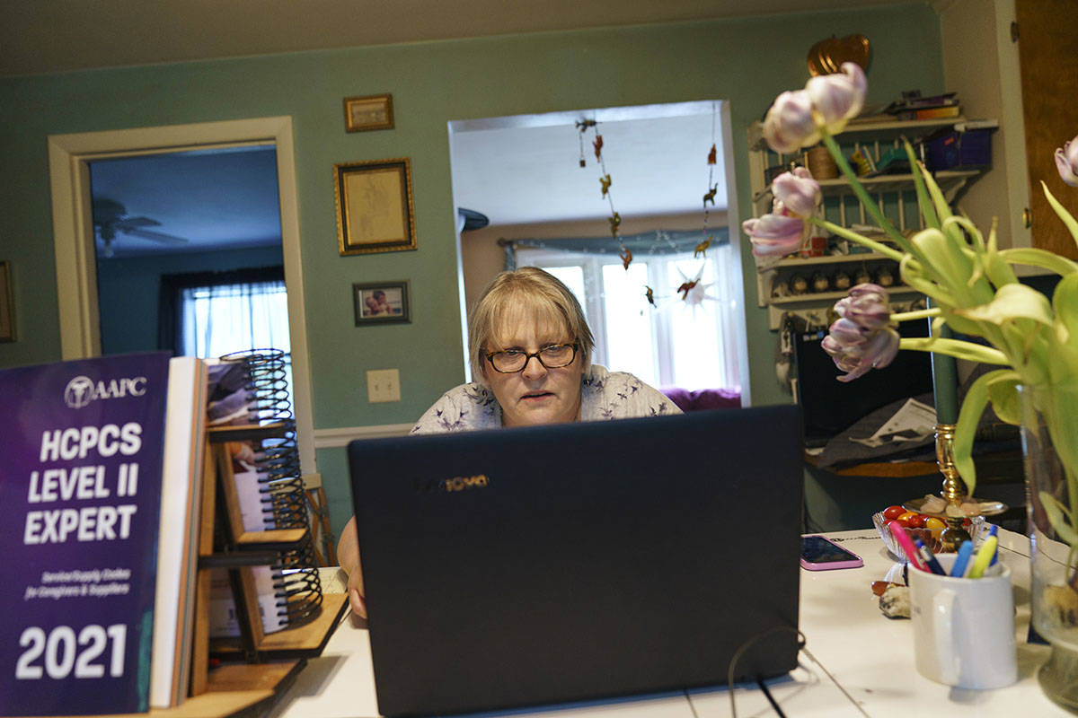 Ellen Booth, 57, studies at her kitchen table to become a certified medical coder, in Coventry, ...