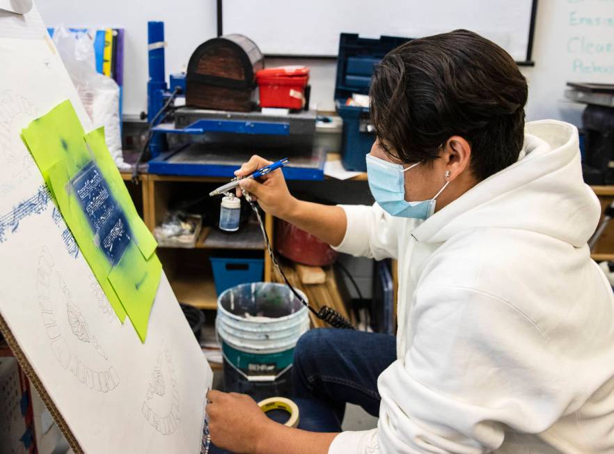Global Community High School senior Edgar Avalos sprays paint over music notes during art class ...