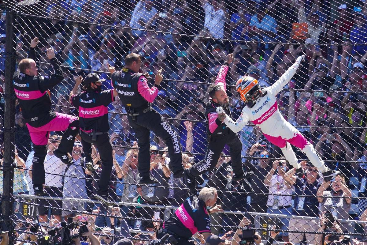 Helio Castroneves of Brazil celebrates with his team as he climbs the fence at the start/finish ...
