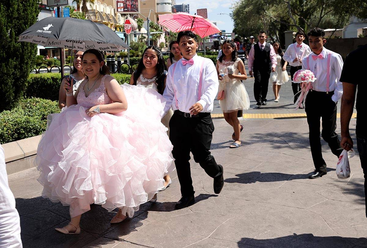 A group stays cool under umbrellas as they pass in front of Caesars Palace on the Strip in Las ...