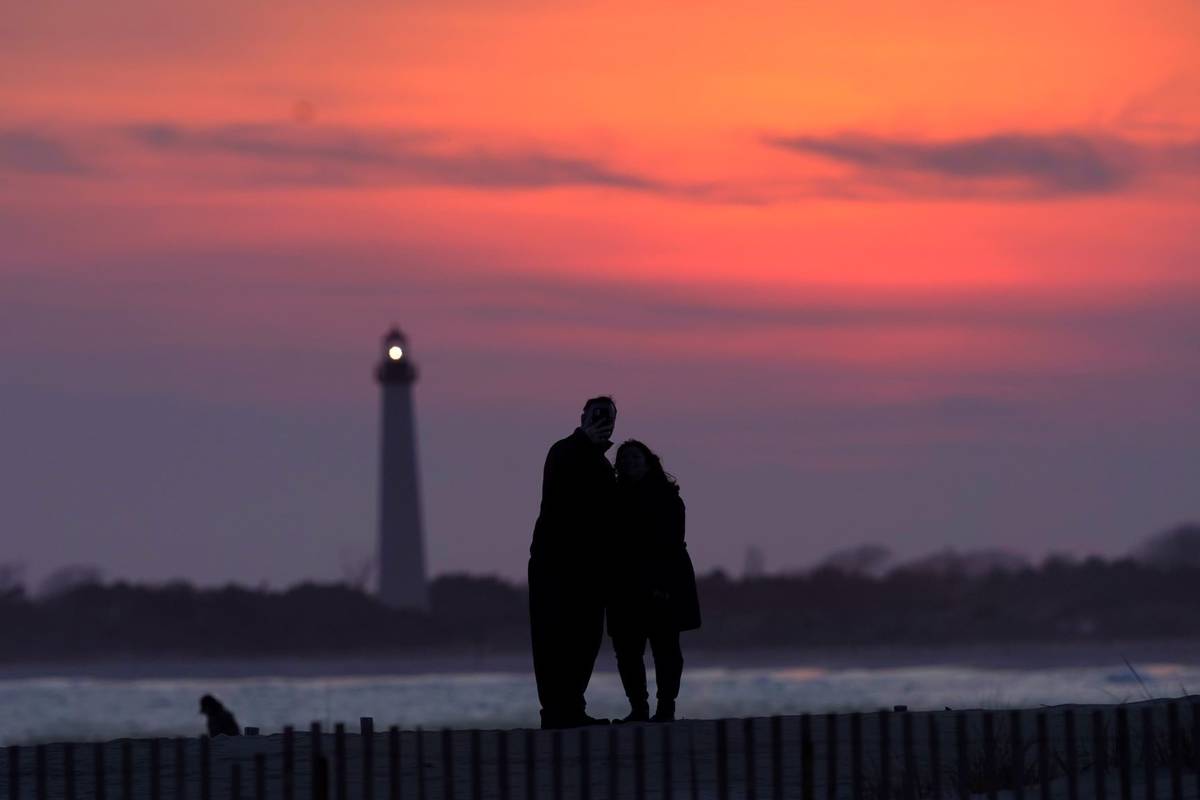 Visitors to Cape May, N.J., watch the sunset behind the Cape May Lighthouse on April 8, 2021.(A ...