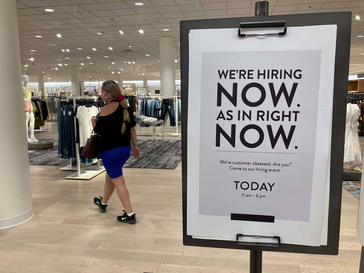 A customer walks behind a sign at a Nordstrom store seeking employees, Friday, May 21, 2021, in ...