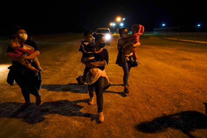 Migrant women carry children in the rain at an intake area after turning themselves in upon cro ...