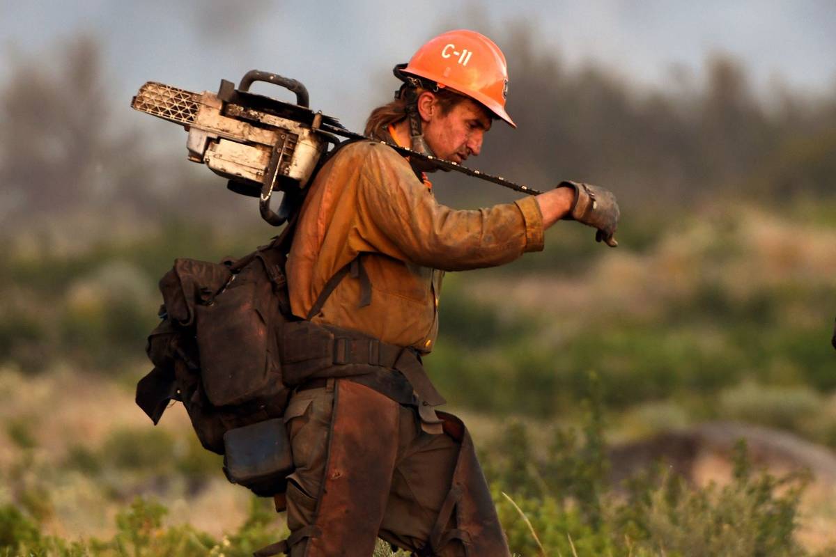 A member of the U.S. Forest Service's Trinity Hotshots firefighting crew carries a chain saw wh ...