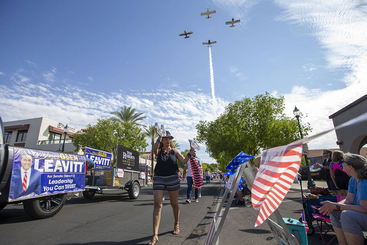 A woman hands out water to onlookers as a flyover with planes manned by the Boulder City Vetera ...