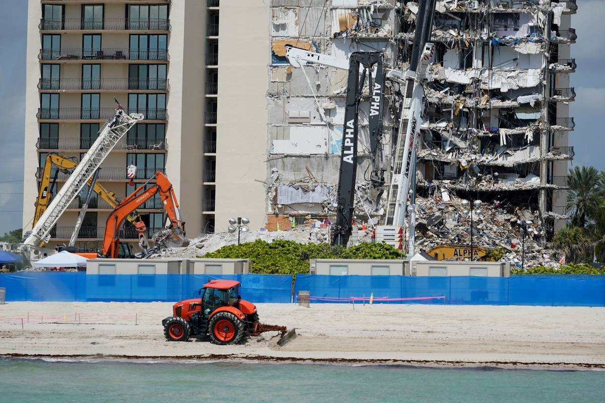 A plow maintains the beach out front as search and rescue personnel work atop the rubble at the ...