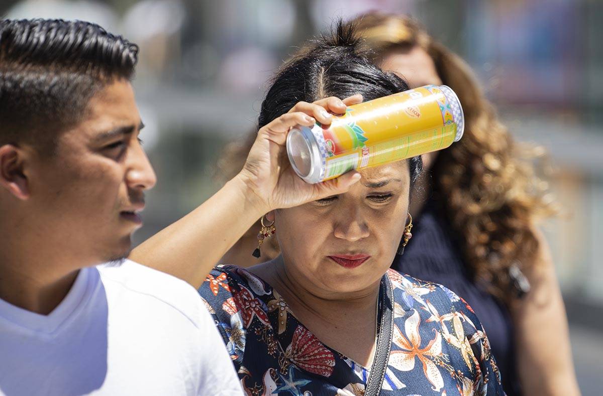A pedestrian places her cold drink on her forehead to cool herself as she walks along Las Vegas ...