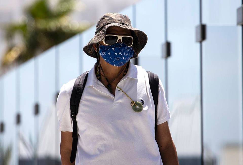 A pedestrian wears a large hat to protect himself from sun as he crosses the pedestrian bridge ...