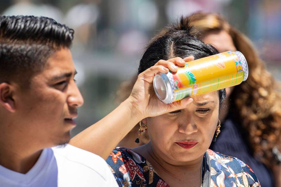 A pedestrian places a can of soda on her forehead to cool herself as she walks along Las Vegas ...