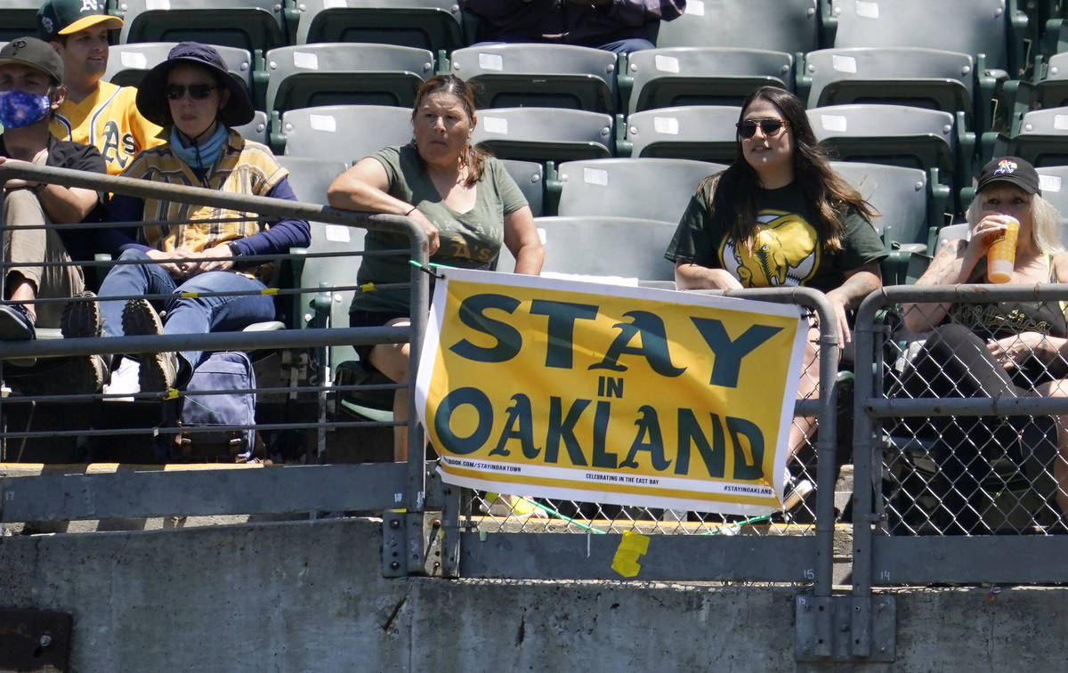 Fans sit behind a sign that reads Stay in Oakland during the first inning of a baseball game be ...