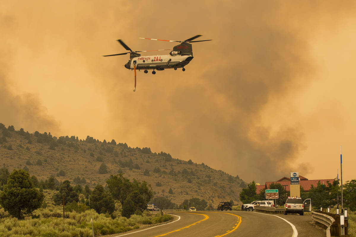 A firefighting helicopter flies as the Tamarack Fire burns around Topaz Lake, Nev., Friday, Jul ...