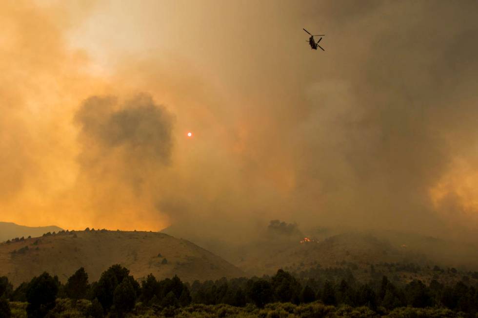 A firefighting helicopter flies as the Tamarack Fire burns around Topaz Lake, Nev., Friday, Jul ...