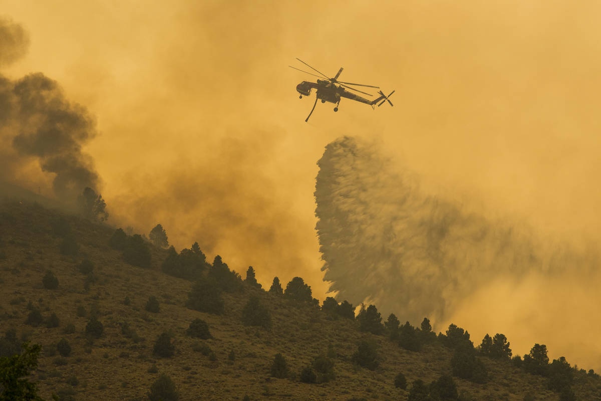 A firefighting helicopter drops water as the Tamarack Fire burns around Topaz Lake, Nev., Frida ...