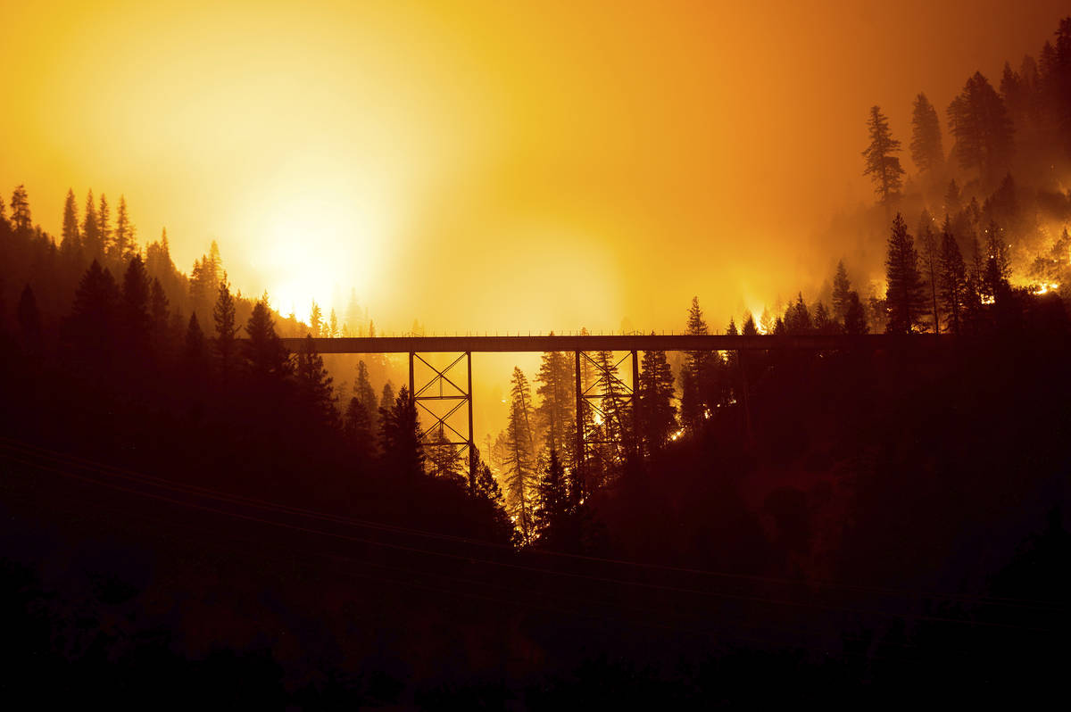 Seen in a long exposure photograph, the Dixie Fire burns behind a bridge in Plumas County, Cali ...