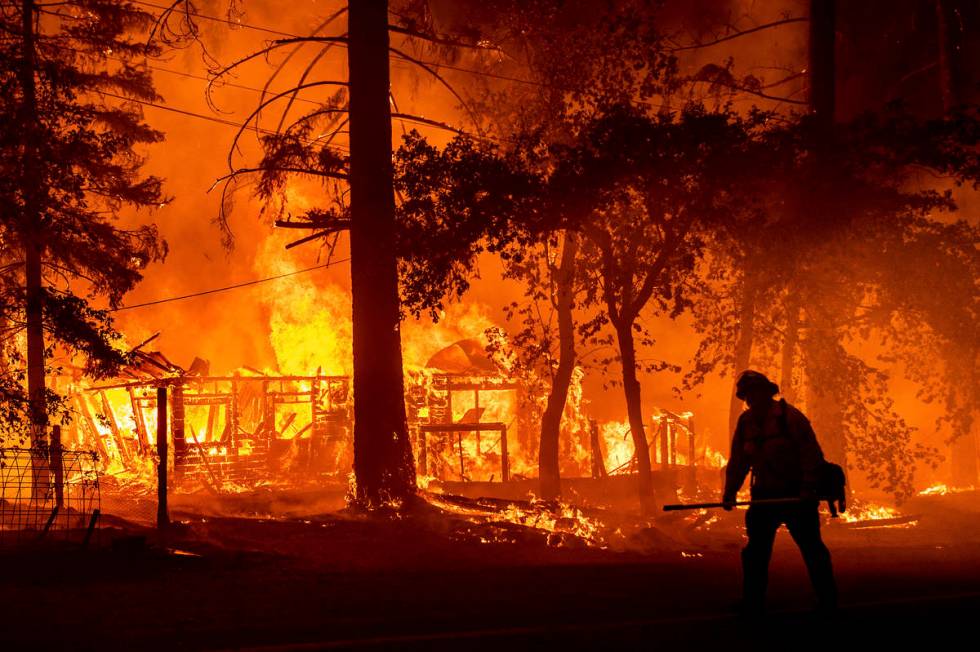 A firefighter passes a burning home as the Dixie Fire flares in Plumas County, Calif., Saturday ...