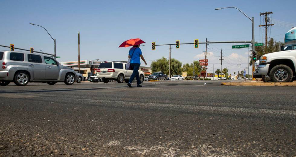 A woman with an umbrella for shade walks at the intersection of North Eastern Avenue and East B ...