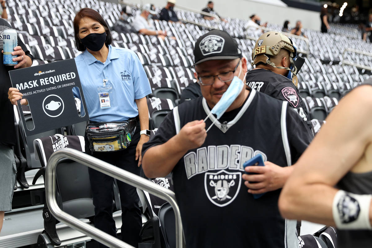 An Allegiant Stadium employee shows a mask required sign to a fan attending a NFL preseason gam ...