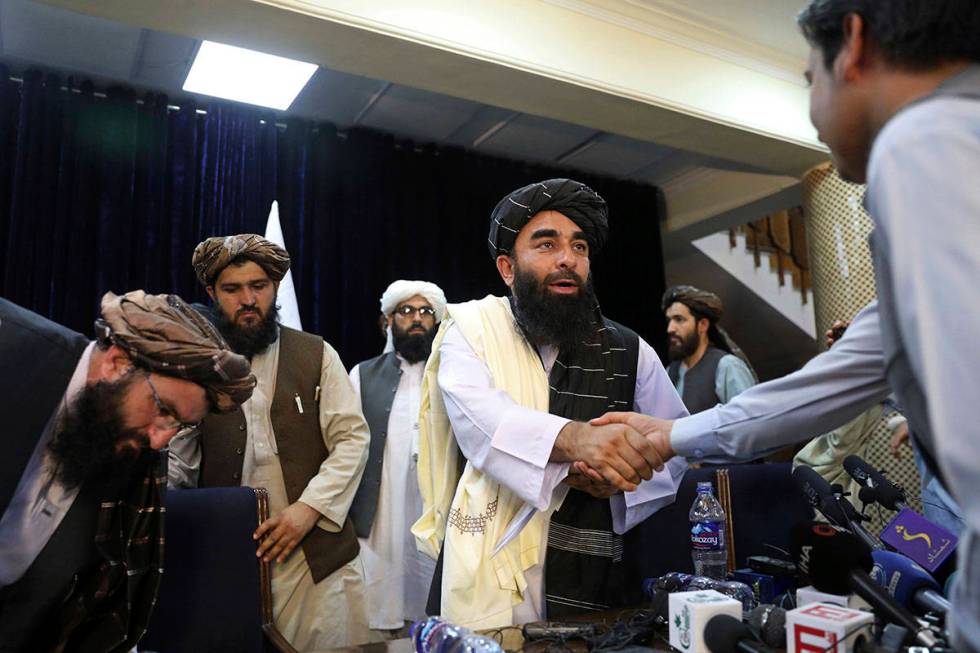 Taliban spokesman Zabihullah Mujahid, shakes hand with a journalist after his first news confer ...