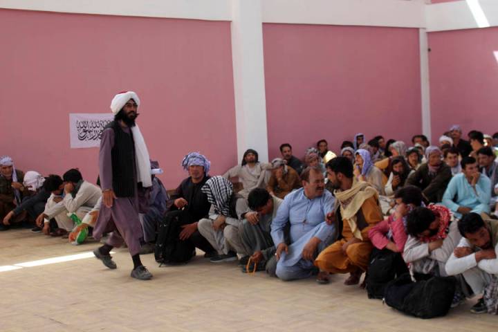 A Taliban fighter stand guard over surrendered Afghan security members forces in the city of Gh ...