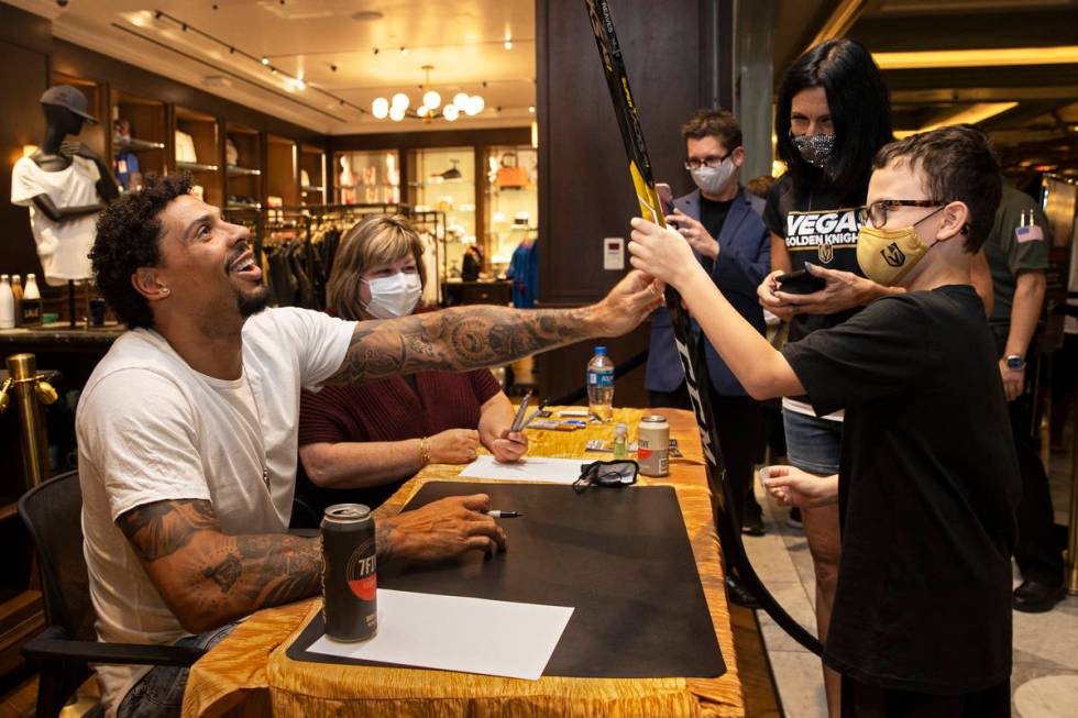 Former Golden Knights player Ryan Reaves, left, signs a hockey stick for Gus Karris, 8, during ...