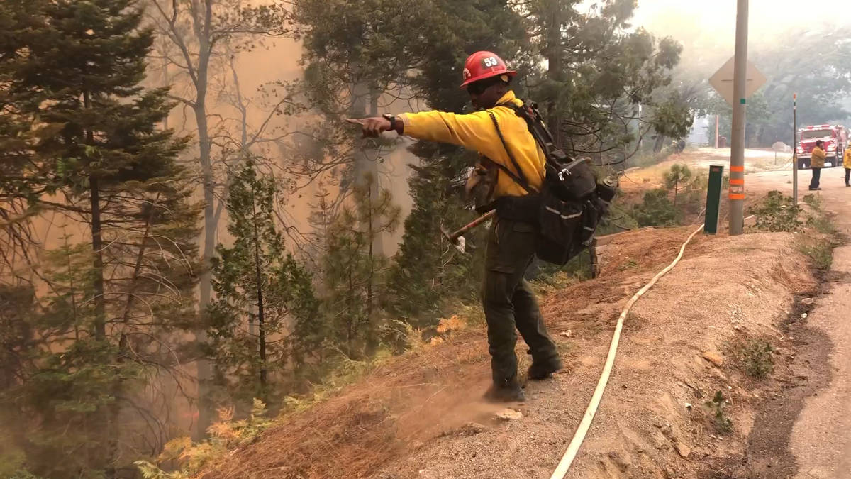 A fire captain points out where crews should carry a hose down a hill as the Caldor Fire burns ...