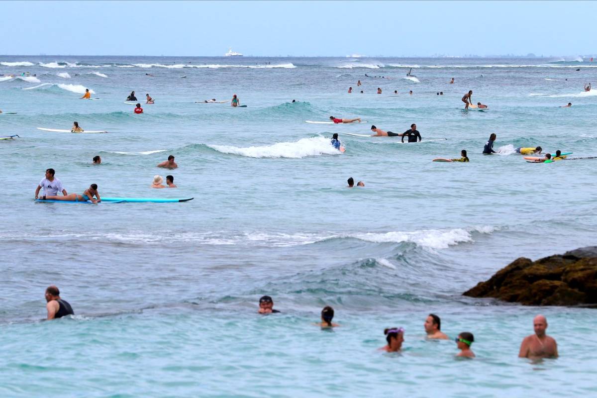 People swim and surf off Waikiki Beach in Honolulu, Tuesday, Aug. 24, 2021. (AP Photo/Caleb Jones)