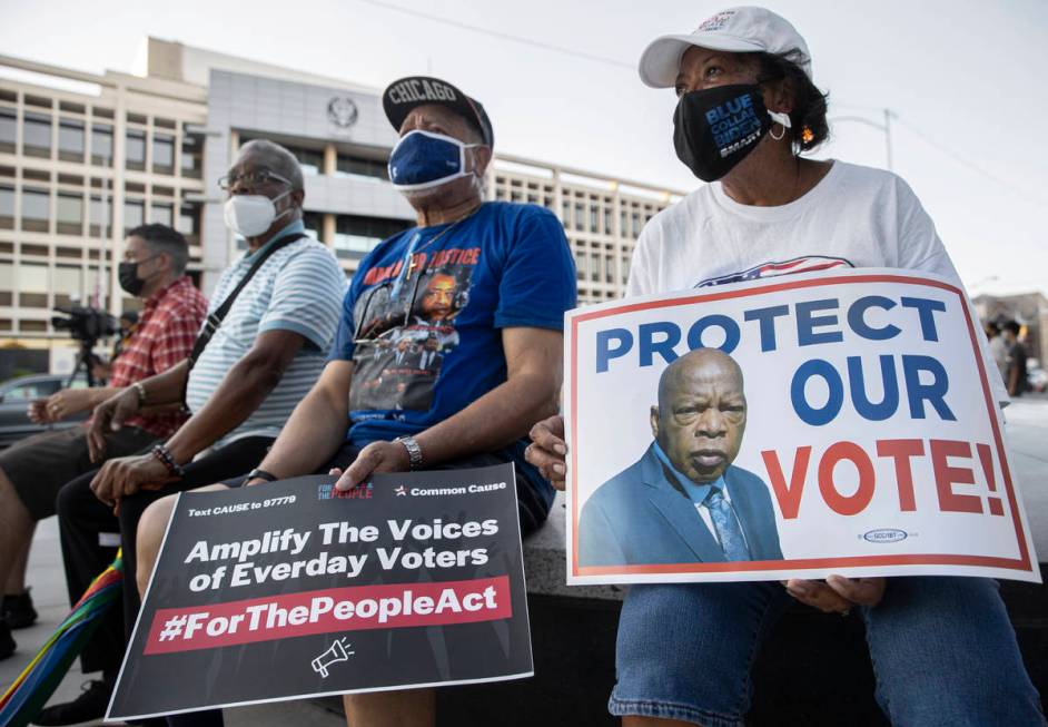 Linda Giddens, right, holds a sign while listening to a speaker during an event against voter s ...