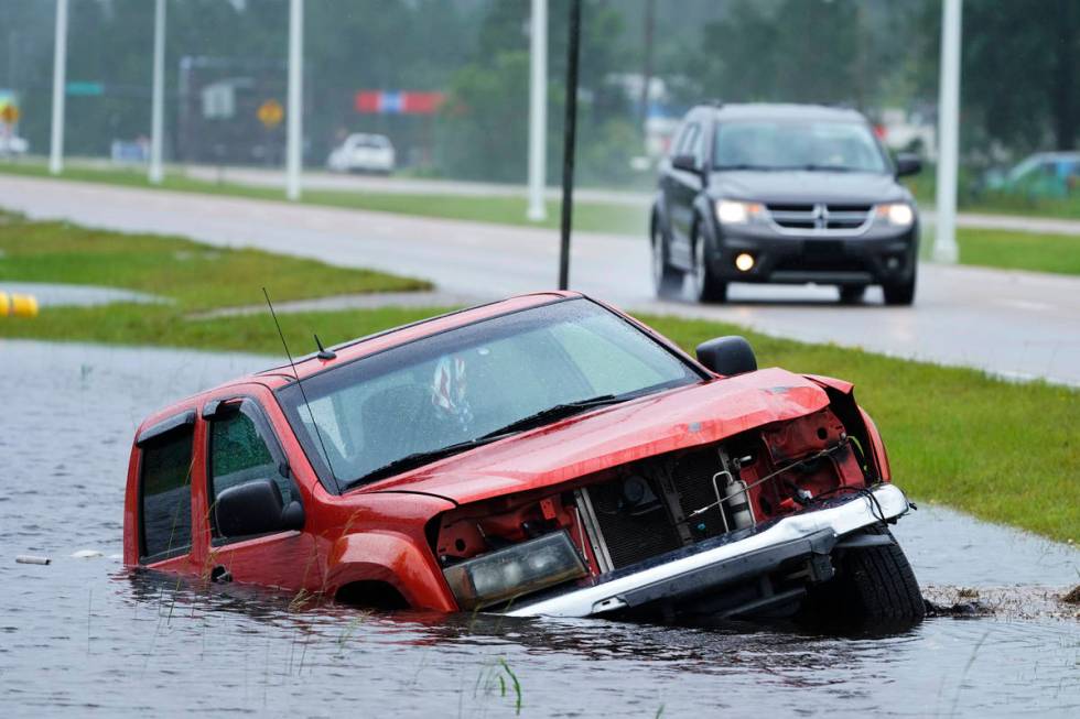 An abandoned vehicle is half submerged in a ditch next to a near flooded highway as the outer b ...