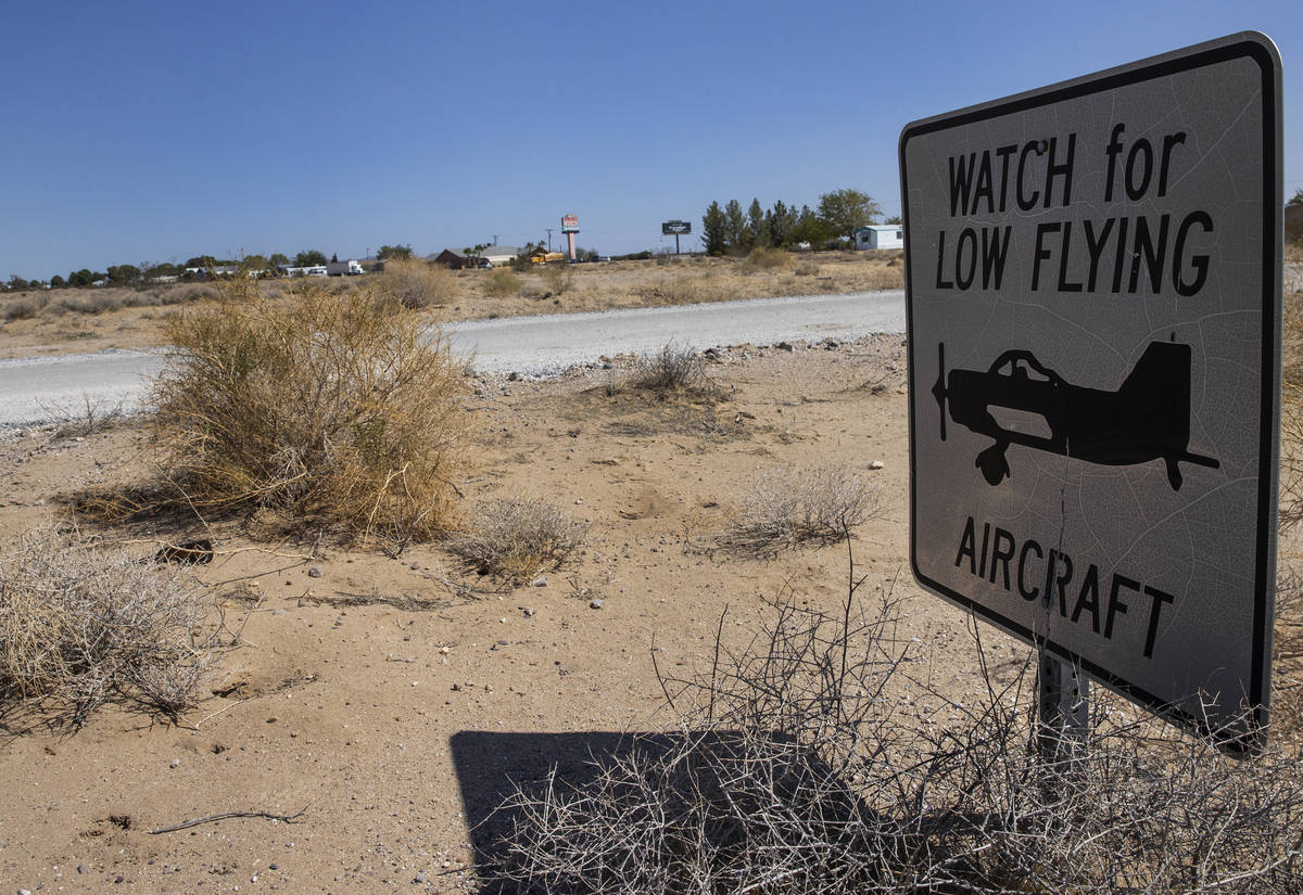 The sign warning residents to watch for low flying aircraft is shown near unpaved airstrip, on ...