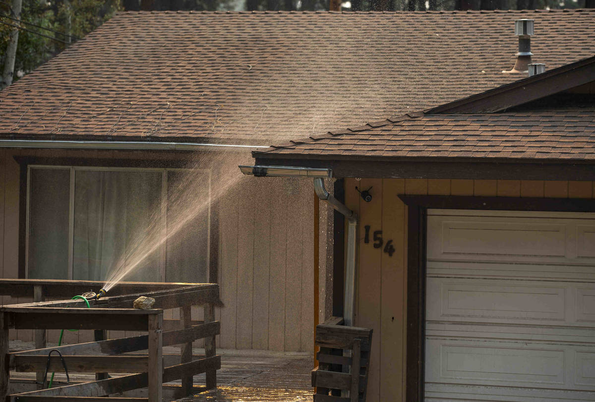 A sprinkler douses an evacuated home from the Caldor Fire on Wednesday, Sept. 1, 2021, in Kings ...