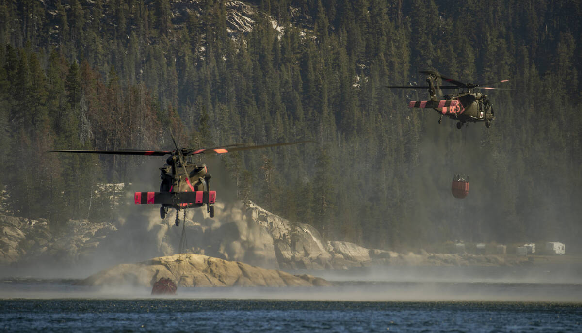 Helicopters scoop up water from Silver Lake to go drop on a nearby ridge as the Caldor Fire con ...