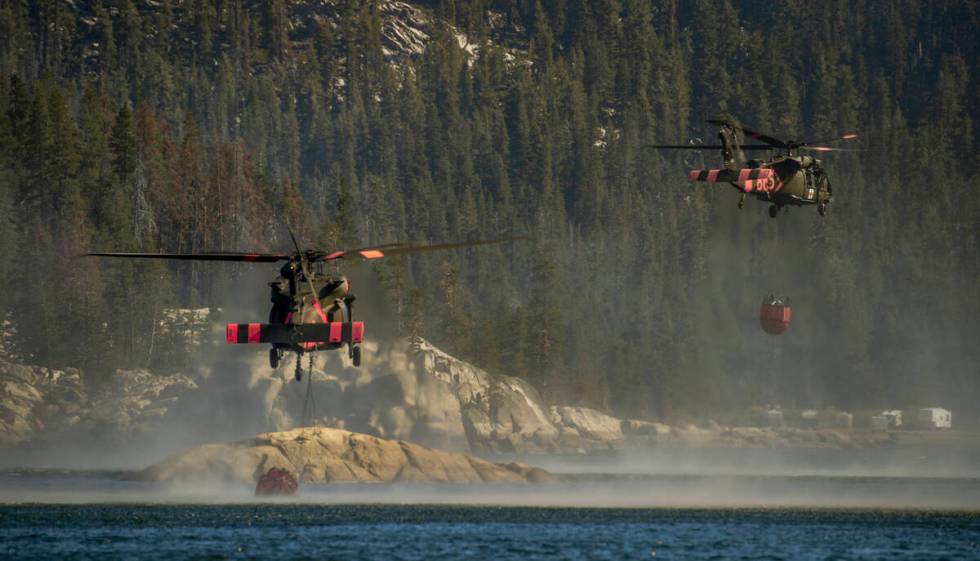 Helicopters scoop up water from Silver Lake to go drop on a nearby ridge as the Caldor Fire con ...