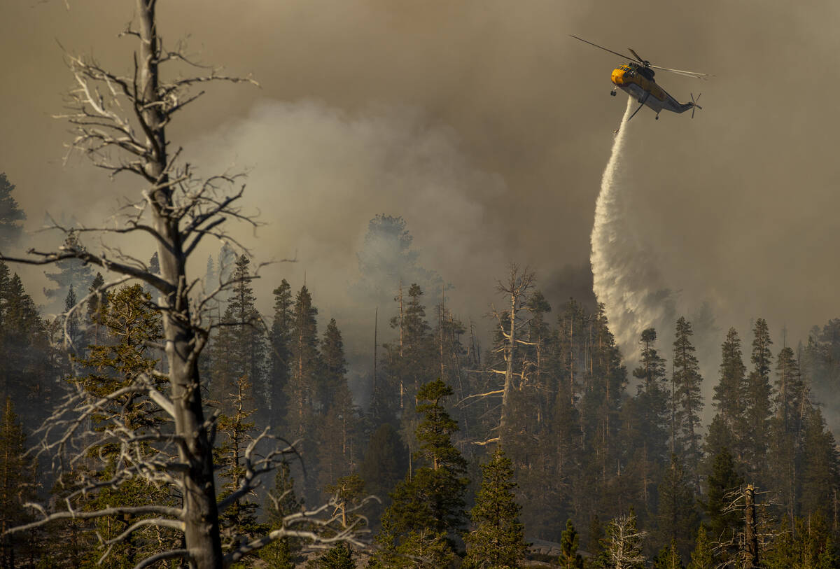 A helicopter drops water from Silver Lake on a burning ridge as the Caldor Fire continues to bu ...