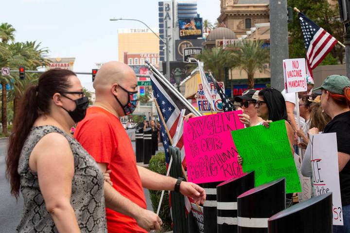 Masked visitors to the Las Vegas Strip pass a group of about 40 protesters calling for an end t ...