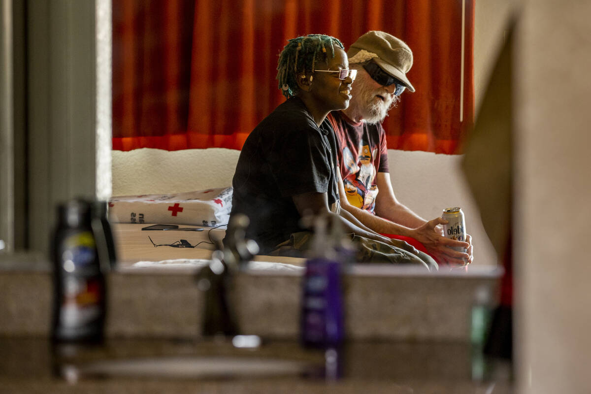 Caretaker Valerie Bridges, left, with Mr. Louis, who is legally blind, sit and talk on a bed in ...