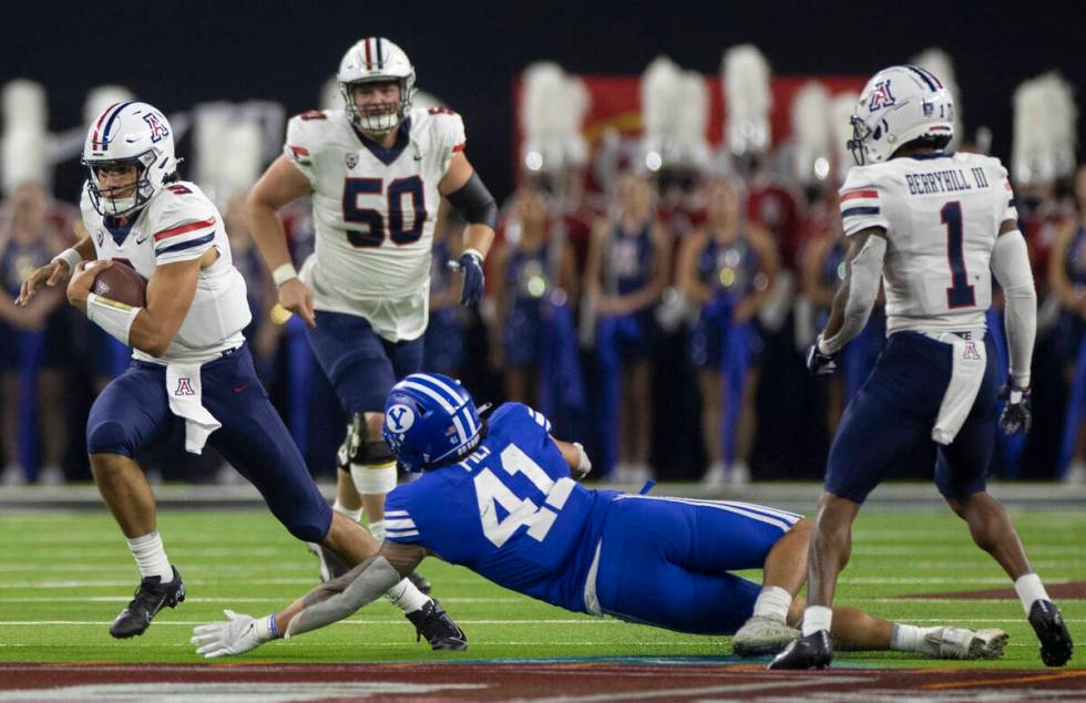 Arizona Wildcats quarterback Gunner Cruz scrambles past Brigham Young Cougars linebacker Keenan ...