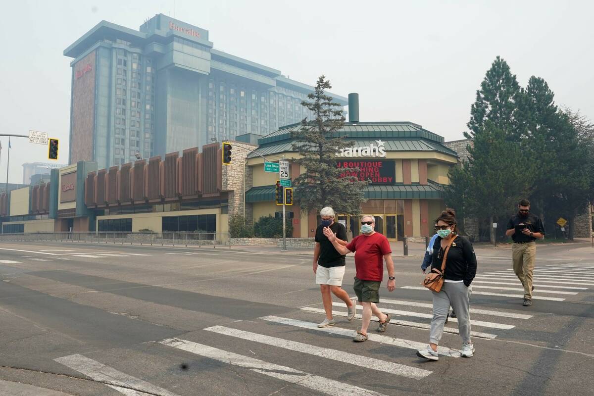 Harrah's Lake Tahoe Casino is shrouded in smoke as face mask wearing pedestrians cross the stre ...