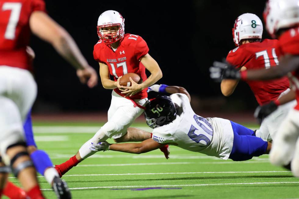 Arbor View's Kyle Holmes (17) looks for an open pas before getting sacked by Steve Manuma (50) ...