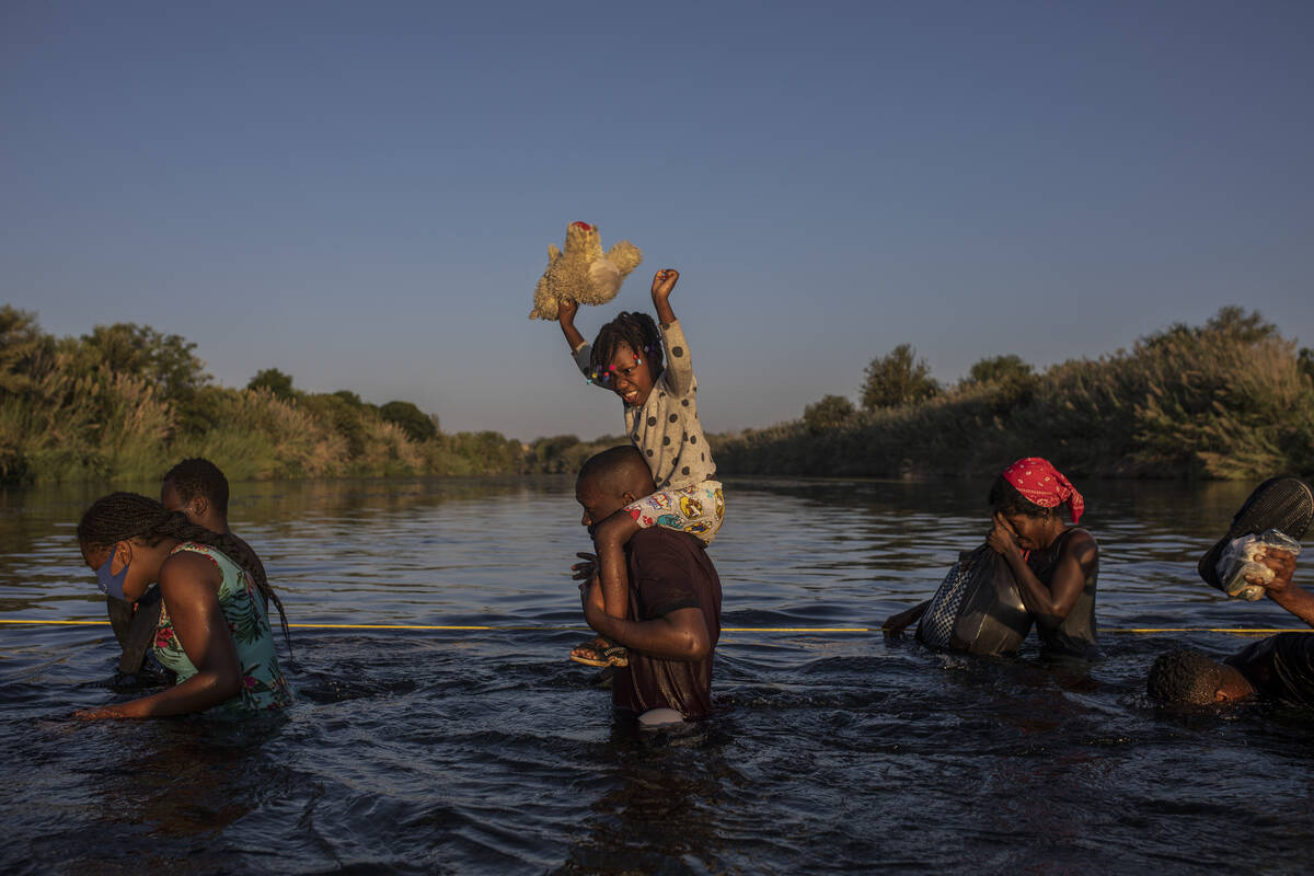 A little girl holds her stuffed animal high above the water as migrants, many from Haiti, wade ...