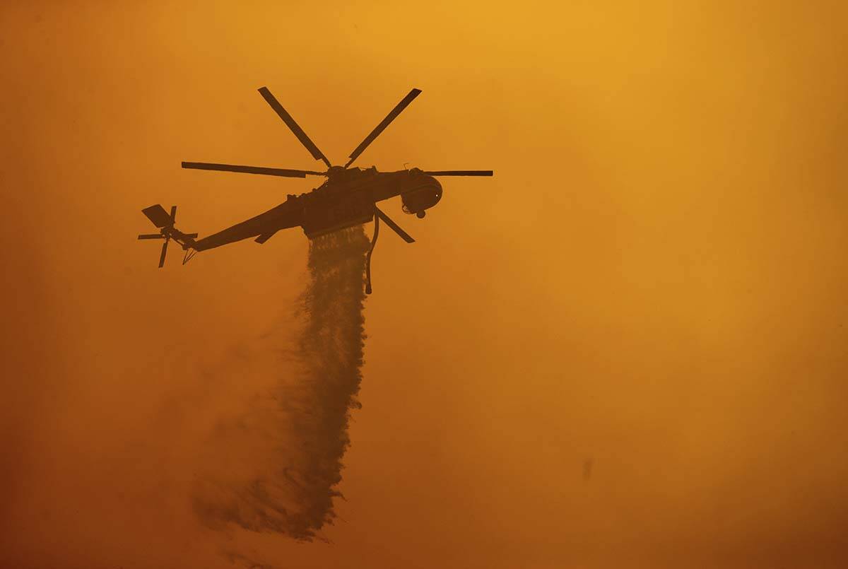 A helicopter drops water on the Fawn Fire burning north of Redding in Shasta County, Calif., on ...