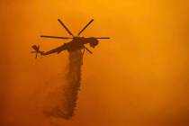 A helicopter drops water on the Fawn Fire burning north of Redding in Shasta County, Calif., on ...