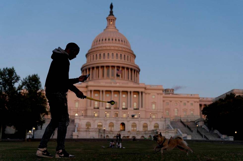 The U.S Capitol is visible at sunset as a man plays fetch with a dog in Washington, Thursday, S ...