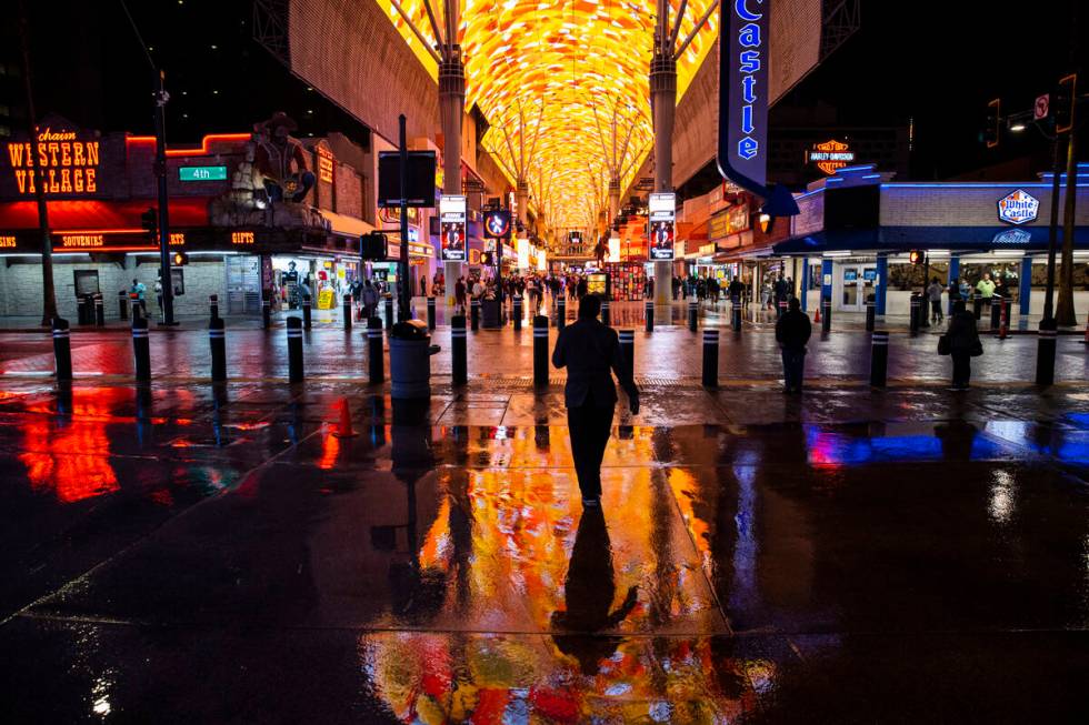 People walk around Fremont Street as the Viva Vision canopy reflects in the street while rain c ...