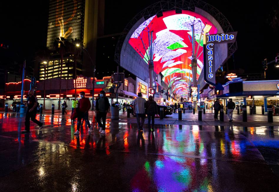 People walk around Fremont Street as the Viva Vision canopy reflects in the street while rain c ...