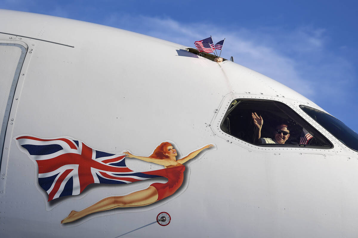 A crew member waves from the cockpit while another holds U.S. flags as Virgin Atlantic Flight 1 ...